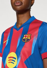 Φανέλα της FC Barcelona με κόκκινες και μπλε κατακόρυφες ρίγες, λογότυπο της Nike, έμβλημα του συλλόγου και κυκλικό λογότυπο της Spotify στο μπροστινό μέρος.