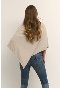 Smėlio spalvos vilnonis pončas su trikampiu raštu, krentantis nuo pečių. Minkšta tekstūra, derinama su mėlynais siaurais džinsais su šoninėmis kišenėmis.