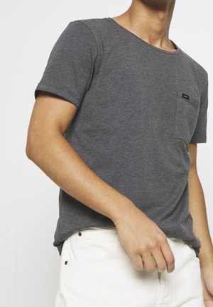 T-shirt gris à manches courtes avec un col rond, doté d'une poche sur la poitrine gauche et d'une petite étiquette noire. Complété par un pantalon blanc.