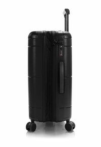 Black hard-shell suitcase with a textured surface, zip closure, combination lock, side handle, and four rolling wheels. Retractable handle on top.