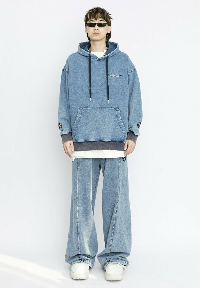 Sudadera de mezclilla con cordones, dos bolsillos frontales y logo; combinada con pantalones de mezclilla de corte holgado. El modelo lleva zapatillas blancas y gafas de sol.