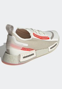 Vit och beige sneaker med mesh-överkropp, vadderad krage, röda detaljer och en texturerad sula med ett mönstrat grepp. Adidas-logotyp på hälen.
