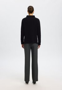 Schwarzer Strickpullover mit hohem Kragen, kombiniert mit grau tailierten Hosen. Das Outfit hat lange Ärmel und eine lockere Passform.