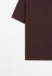 Maglietta a maniche corte marrone realizzata in morbido materiale in cotone misto. Presenta una vestibilità rilassata e orlo dritto. Senza motivi o decorazioni.