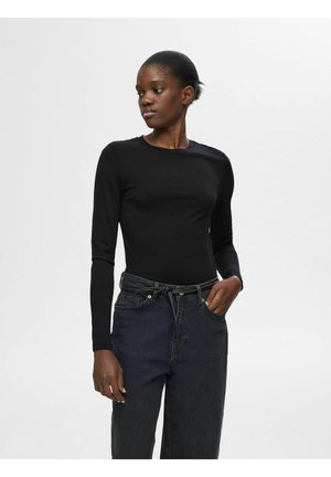 Sort langærmet top med rund halsudskæring, parret med højtaljede mørke denim jeans med en bundet talje. Glat, tætsiddende tekstur.