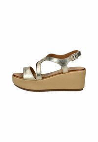 Metalické stříbrné wedge sandály s křížovými pásky a přezkou na kotníku, s lehkou béžovou platformou a hladkou koženou texturou.