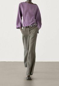 Haut ample violet avec un décolleté asymétrique, associé à un pantalon large taille haute de couleur vert olive clair et des sandales noires simples.