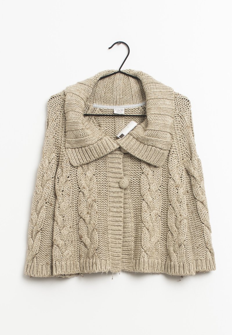 Cardigan beige tricoté avec un large col, orné de motifs torsadés, une fermeture par un bouton unique et des bords côtelés. Suspendu à un crochet noir.