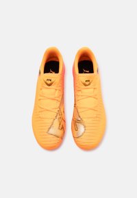 Scarpe da calcio arancioni brillanti con tomaia testurizzata, caratterizzate da accenti di design a strisce nere e un sistema di allacciatura centrale.