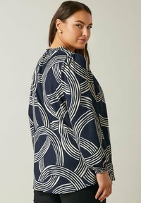 Marinebluse mit weißem, abstraktem Streifenmuster, langen Ärmeln, gerafftem Halsausschnitt und elastischen Bündchen. Weicher, strukturierter Stoff mit lockerer Passform.