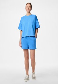 T-shirt bleu clair à manches courtes avec une coupe décontractée, associé à un short bleu à cordon assorti. Matériau en coton, texture lisse, design décontracté.