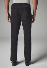 Brown tailored pants with a straight-leg design, featuring two back pockets and a smooth texture. Finished with a black waistband and shiny shoes.