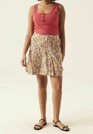 Lyserød ribbet tanktop med tre knapper, parret med en svingende blomsterkjole med gule, lyserøde og grønne mønstre. Sorte flade sandaler.