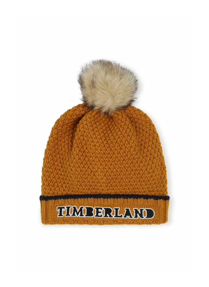 Bonnet tricoté en jaune moutarde avec un motif texturé, doté d'un pompon en fausse fourrure sur le dessus et d'une bande noire avec le logo "TIMBERLAND".