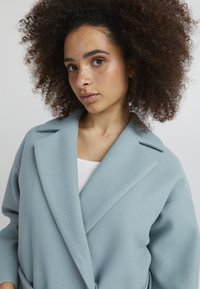 Manteau oversize bleu clair avec une finition douce et texturée, présentant un col cranté et une silhouette décontractée.