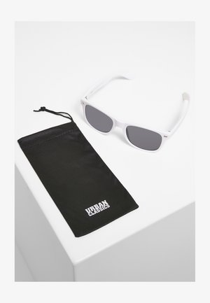 Valged plastikust prillid hallide läätsedega musta kangast kotikese kõrval, millel on tugeva kirjatüübiga valge "URBAN CLASSICS" logo.