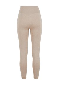 Leggings beiges côtelés avec une taille haute. Le tissu semble doux, texturé avec des lignes verticales, et ajusté sur l'ensemble des jambes.