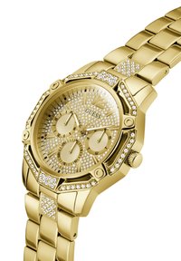 Montre dorée avec un boîtier octogonal, incrusté de cristaux, cadran texturé et trois sous-cadrans. Le bracelet est composé de segments dorés plats et reliés.