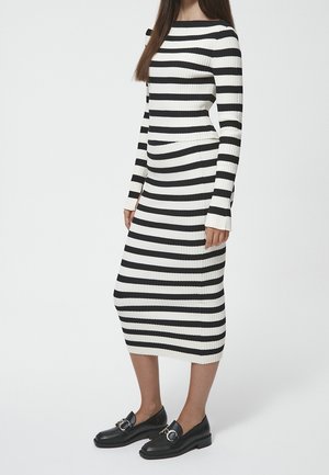 Robe côtelée à rayures noires et blanches avec des manches longues et un décolleté bateau. Associée à des mocassins noirs avec des détails en métal argenté.