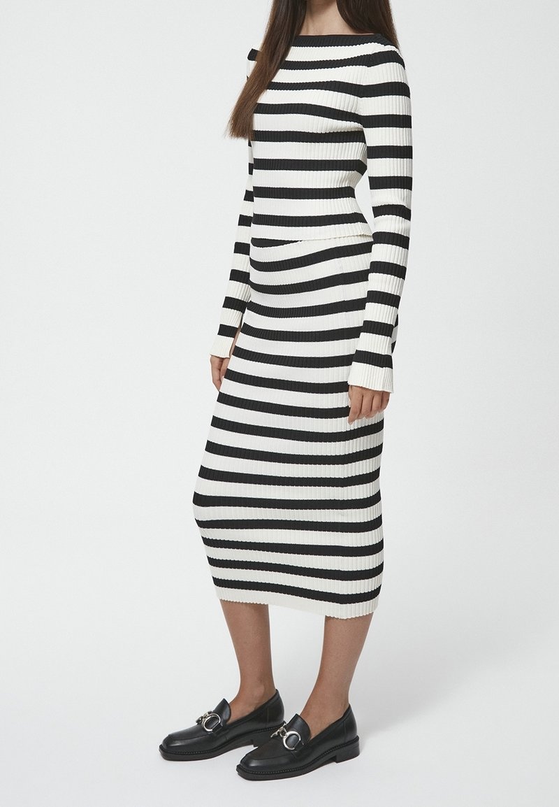 Robe côtelée à rayures noires et blanches avec des manches longues et un décolleté bateau. Associée à des mocassins noirs avec des détails en métal argenté.