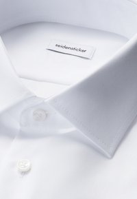 Camicia bianca con colletto a punta e bottoni, con etichetta del marchio "seidensticker" visibile all’interno del colletto.