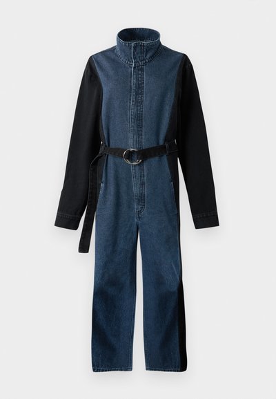 Salopette in denim con colletto alto, maniche lunghe nere, vita con cintura e fibbia circolare, e un design a blocchi di colore in tonalità blu.