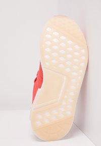 Červená teniska s texturovaným svrškem a průhlednou gumovou podrážkou s diamantovým vzorem pro lepší trakci. Patní část je bílá.