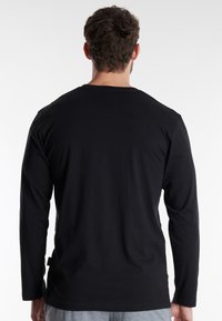 Schwarzes langärmliges Shirt aus weichem Baumwollmaterial. Verfügt über einen klassischen Rundhalsausschnitt und eine lockere Passform mit geraden Ärmeln.