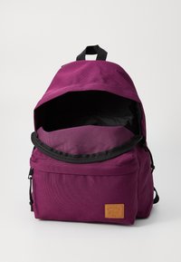Sac à dos en tissu violet avec fermeture éclair et accents noirs, doté d'un grand compartiment principal et d'une petite poche avant avec logo.