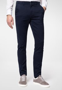 Granatowe, dopasowane chinosy z bawełny z przednimi kieszeniami i zamkiem błyskawicznym. W połączeniu z szarymi sneakersami z białymi sznurówkami i teksturowanym wykończeniem.