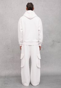 Sudadera de algodón blanca con un corte relajado y capucha ajustable, combinada con pantalones cargo de pierna ancha que cuentan con bolsillos laterales. Textura suave.