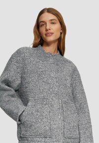 Grau strukturierte Jacke mit Rundhalsausschnitt, frontalen Taschen und lockerer Passform. Der Stoff hat ein gemütliches, weiches Erscheinungsbild.