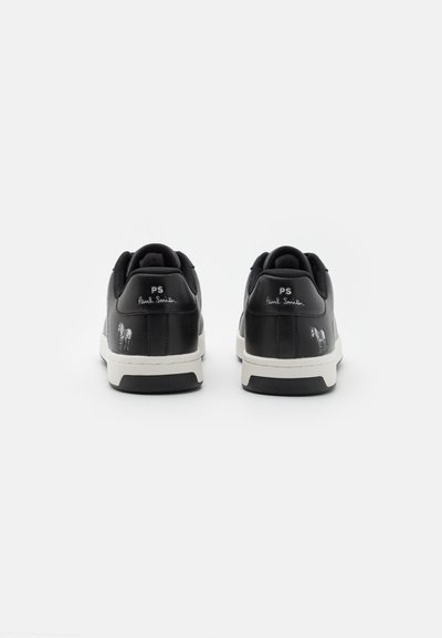 Black leather sneakers with white sole, featuring a minimalist design and embossed logo on the back. Textured accents on the heel.