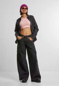 Zwarte denim wijde cargo broeken en een zwart button-up jasje, gecombineerd met een roze crop top, zwarte chunky schoenen en een paarse beanie.