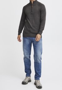 Ciemnoszary sweter z zamkiem pod szyją, z prążkowanymi mankietami i dolnym brzegiem, zestawiony z jasnoniebieskimi dżinsami oraz szarymi butami sportowymi z teksturowaną podeszwą.