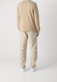 Beige sweatshirt med långa ärmar, ihop med beige bomullsbyxor och vita sneakers, sedd bakifrån mot en enkel bakgrund.