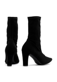 Czarne, zamszowe botki sięgające kostki z dopasowaną cholewką, spiczastym noskiem i średnim obcasem. Posiadają przeszyte detale wzdłuż szwu oraz gładkie wykończenie.