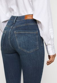 Smaltsiddende jeans i mørkeblå denim med høj talje, der har en brun læderlap bagpå og diskrete syninger på lommerne.