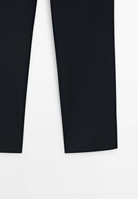 Partie inférieure d'un pantalon noir fuselé montrée sur fond blanc.