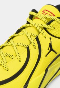 Κίτρινο αθλητικό παπούτσι με μαύρες λεπτομέρειες, κατασκευασμένο από υλικό με υφή, με ξεχωριστό κορδόνι και έντονο λογότυπο. Τολμηρός σχεδιασμός με αθλητικά στοιχεία.