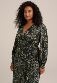 Rochie verde din material moale, cu un model floral în nuanțe de violet și galben, mâneci lungi bufante și detaliu cu curea la talie.