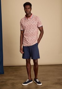 Polo shirt met korte mouwen in koraal met een wit golfpatroon, contrast kraag, gecombineerd met marineblauwe shorts en marineblauwe sneakers.