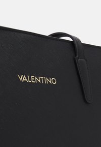 Black leather tote bag featuring a textured finish, gold "Valentino" logo, and a top handle for carrying.