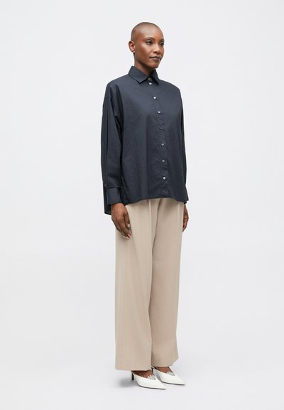 Tmavomodrá košeľa na gombíky s golierom, voľný strih, dlhé rukávy, kombinovaná so svetlými nohavicami s širokými nohavicami a bielymi lodičkami s ostrou špičkou.