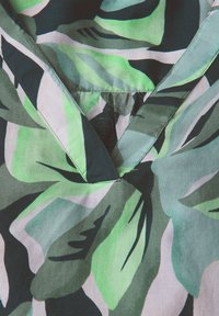 Tissu vert et noir à motifs avec des designs de feuilles abstraites, featuring un décolleté en V et une texture douce et lisse. Pas de matériel visible.