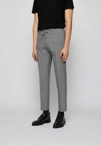 Grå skräddarsydda byxor med snörning i midjan, slim fit och subtil textur. Matchas med svarta skor och en svart T-shirt.