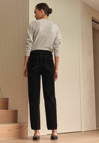 Grijs gespikkeld trui, zwarte corduroy broek, slim recht gesneden, en lage hakken met een textuurriem, tegen een neutrale achtergrond.