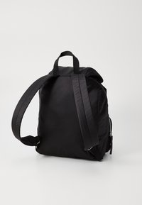 Zaino nero in nylon con spallacci regolabili, maniglia superiore e tasca con zip. Texture liscia, design minimalista, forma arrotondata.
