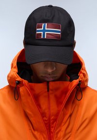 Svart keps med en upphöjd norsk flagga patch, bärs under huvan på en klar orange jacka med dragkedjestängning och snörning.
