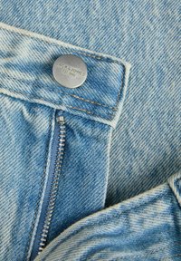 Vaqueros de mezclilla de un azul claro con un botón plateado de la marca "JACK & JONES" y un cierre de cremallera. La tela presenta un patrón texturizado y descolorido.